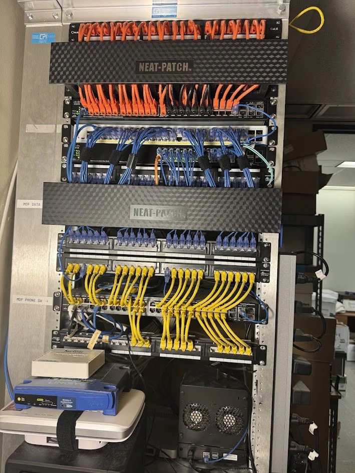A network patch panel cabled and dressed by Enlighten, with orange, blue and yellow cable runs.